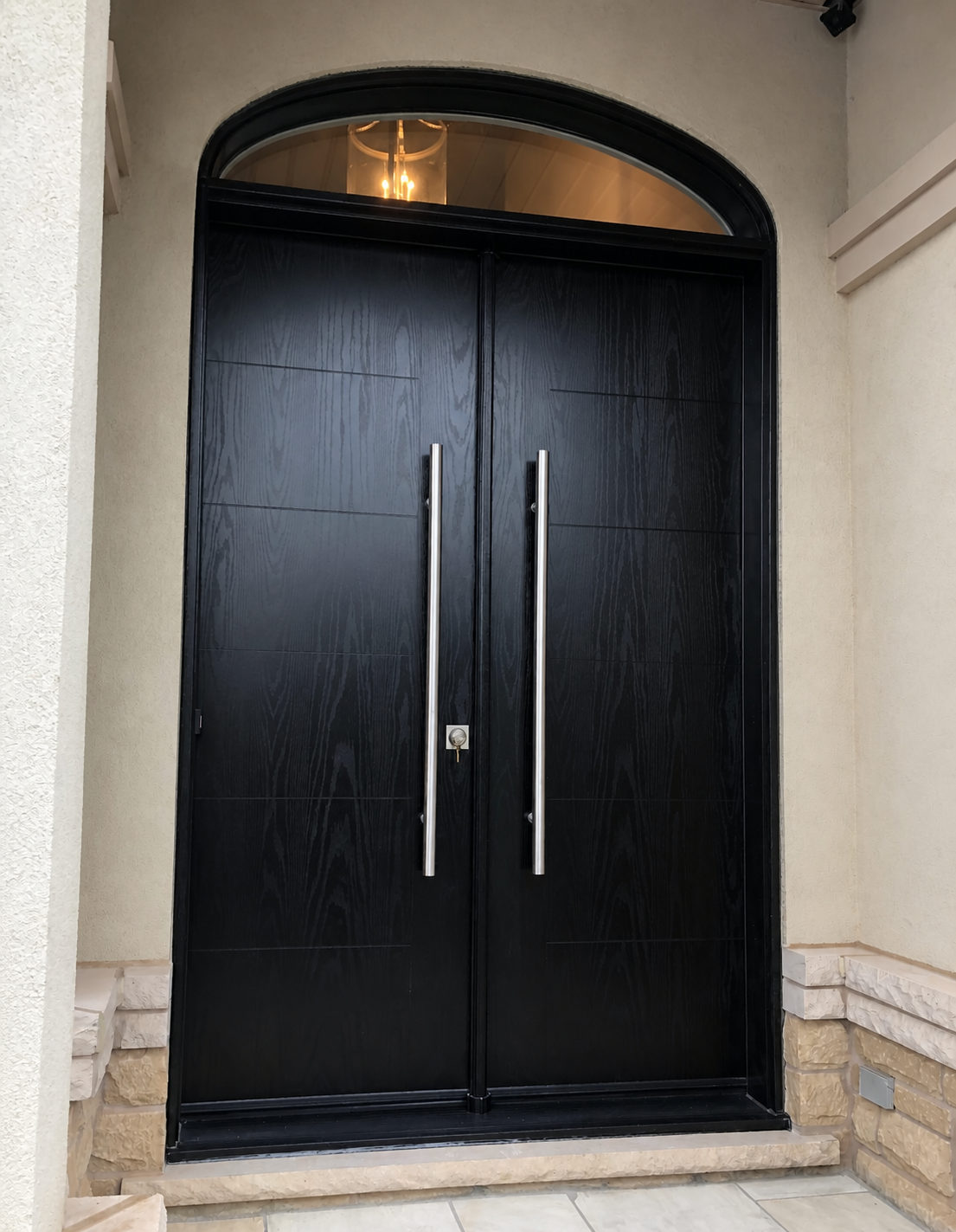 Black woodgrain double entry doors with tall stainless steel pull handles below a curved arched glass transom