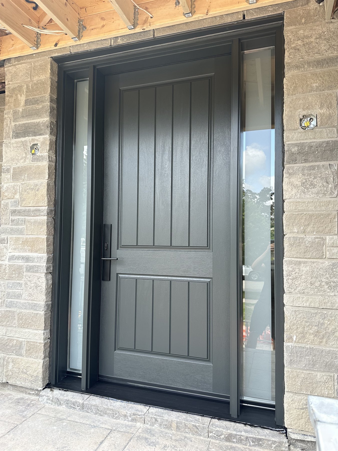 Single dark entry door with two narrow glass sidelites in the same stone opening