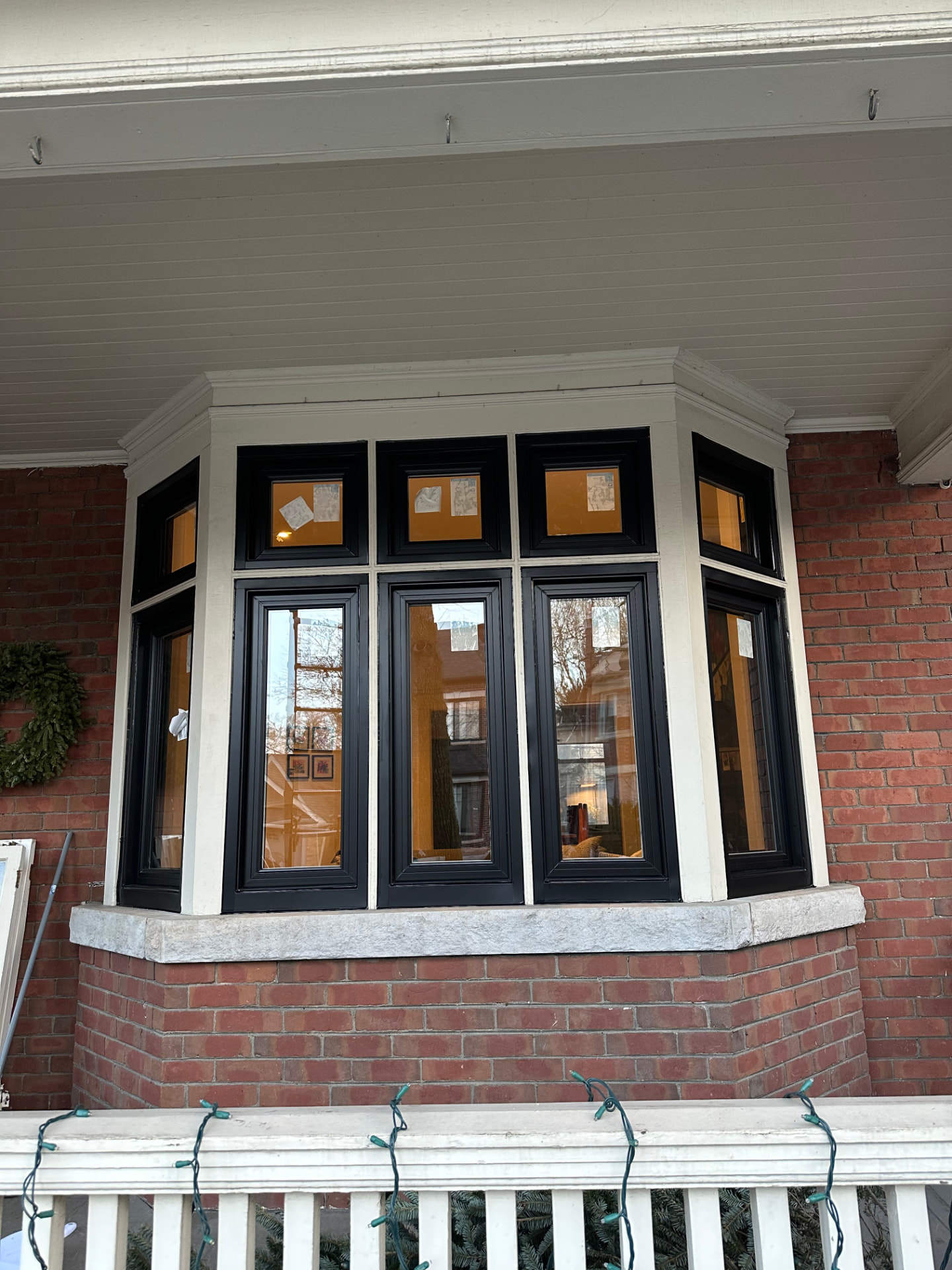 Black-framed bay window with three tall panes and square transom lights above, set in a red brick porch wall with a stone sill