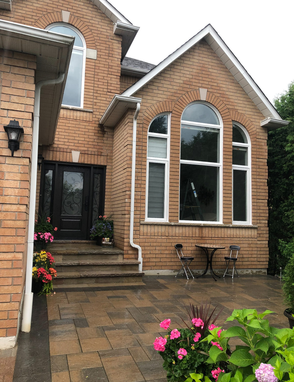 Brick house gable with a large arched white-framed window unit and a second arched window over the entry