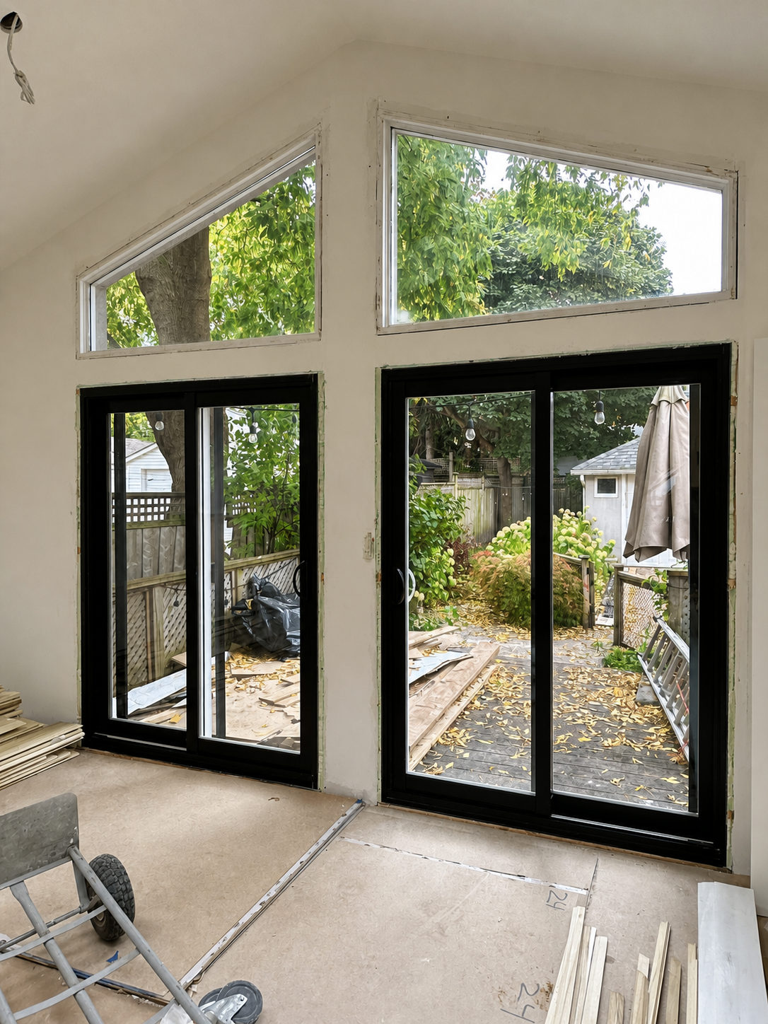 Interior view of two new black-framed sliding patio doors with transom windows above, installed and awaiting trim
