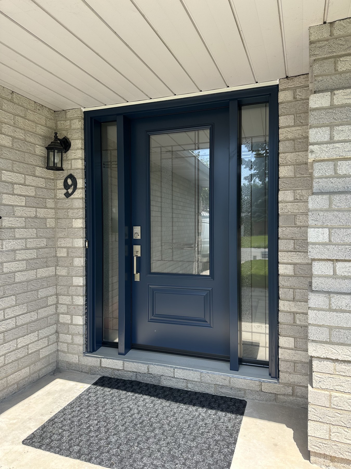 New dark blue entry door with decorative glass sidelites in the same brick porch