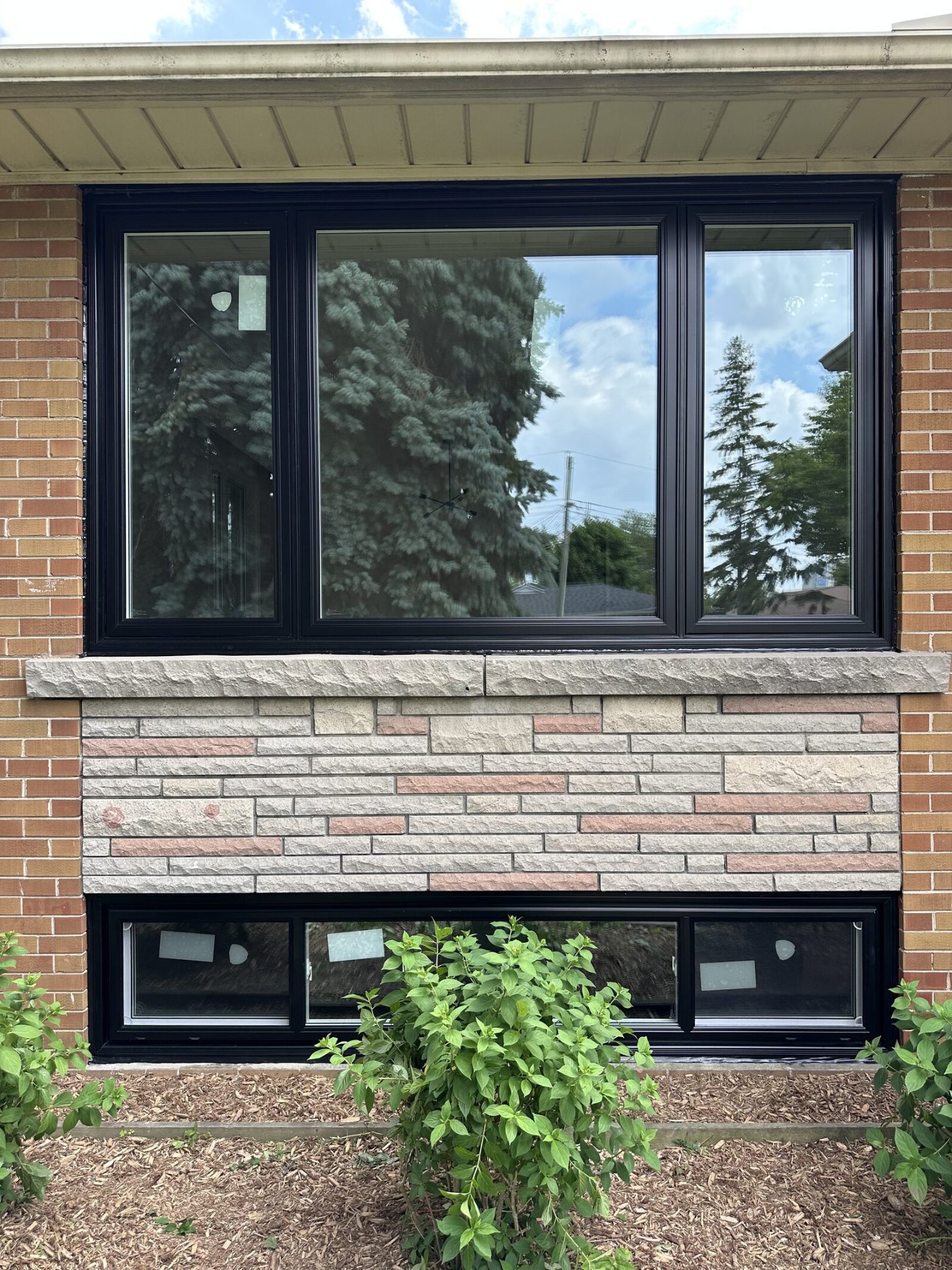 Rear elevation of a brick home with newly installed black-framed windows above a wood deck