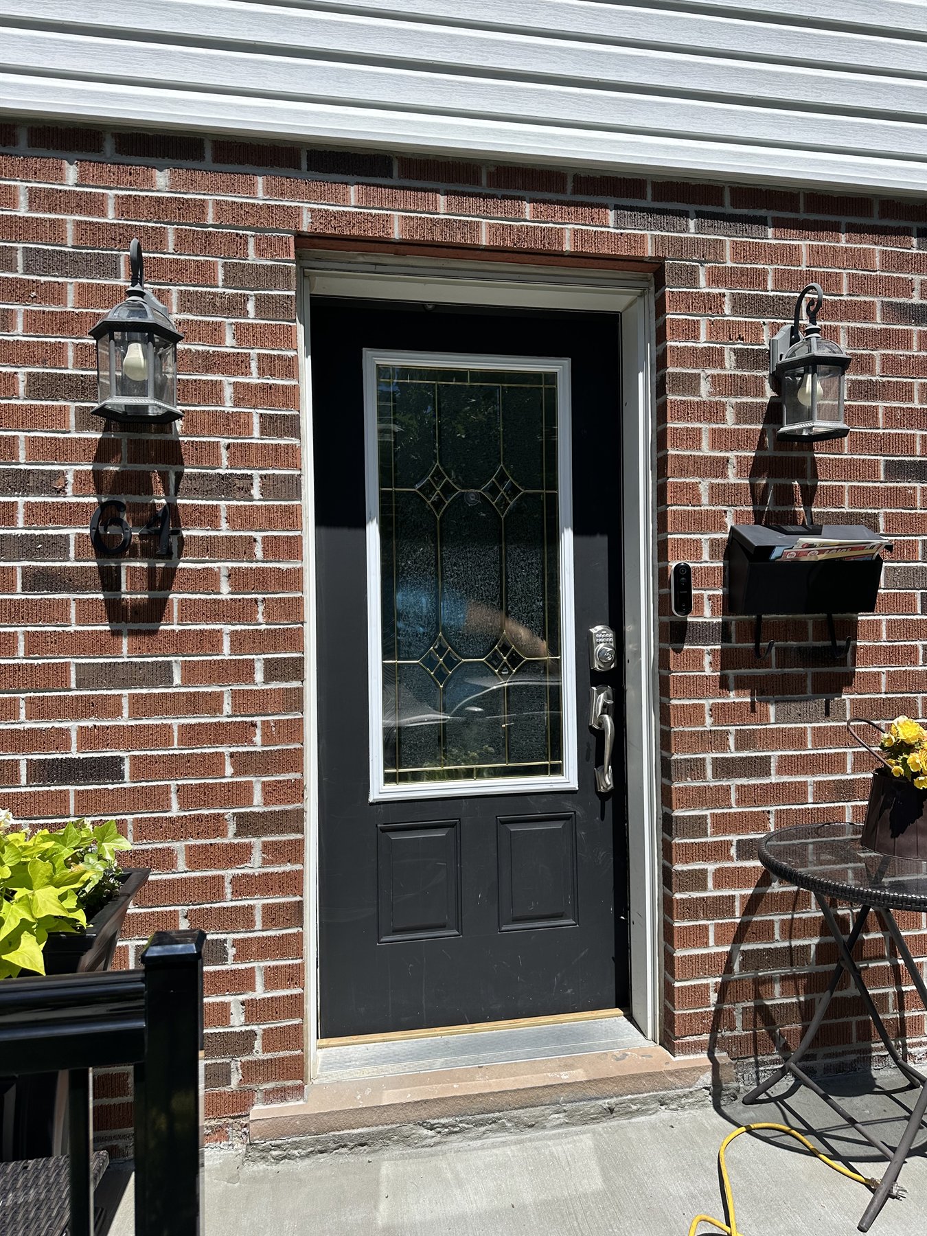 Black entry door with a single decorative leaded glass panel in a red brick wall