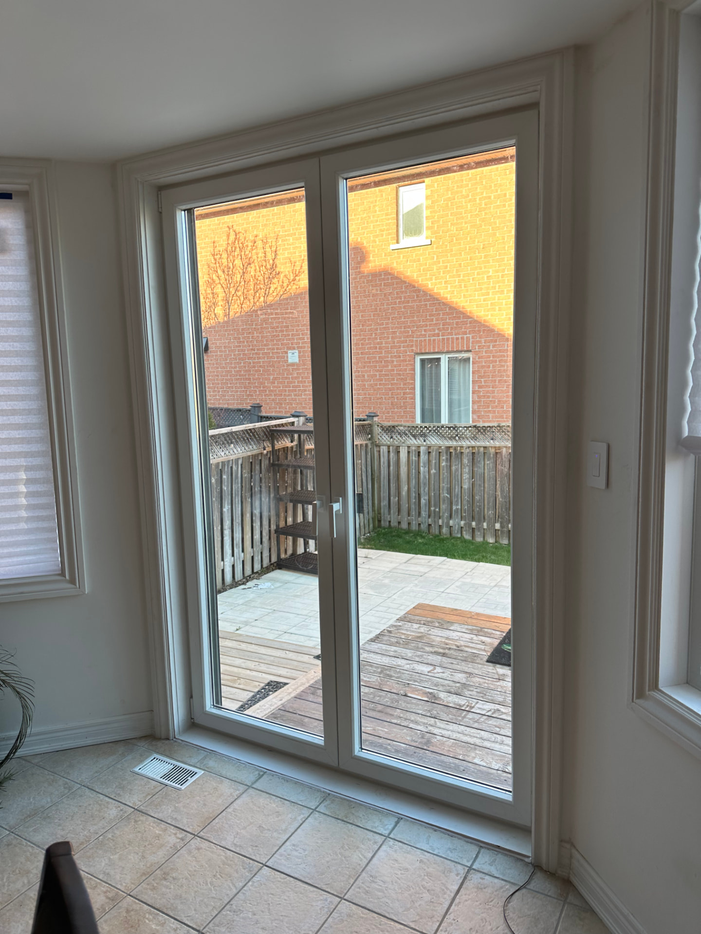 Interior view of a two-panel European door with full-height glass and a white handleset, in a tiled room looking onto a fenced backyard