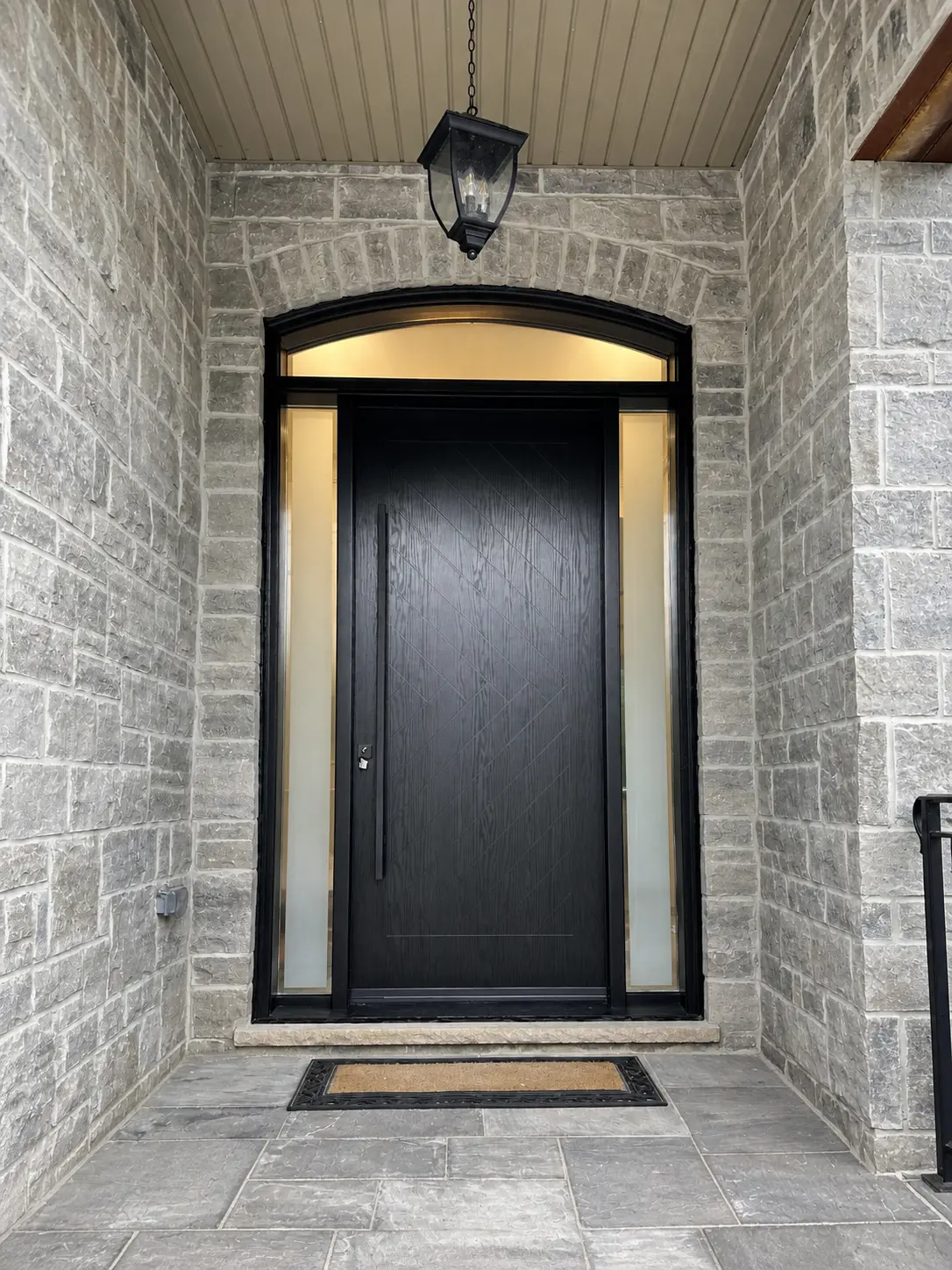 Single black entry door with two frosted sidelites set in a stone porch opening with an arched transom above