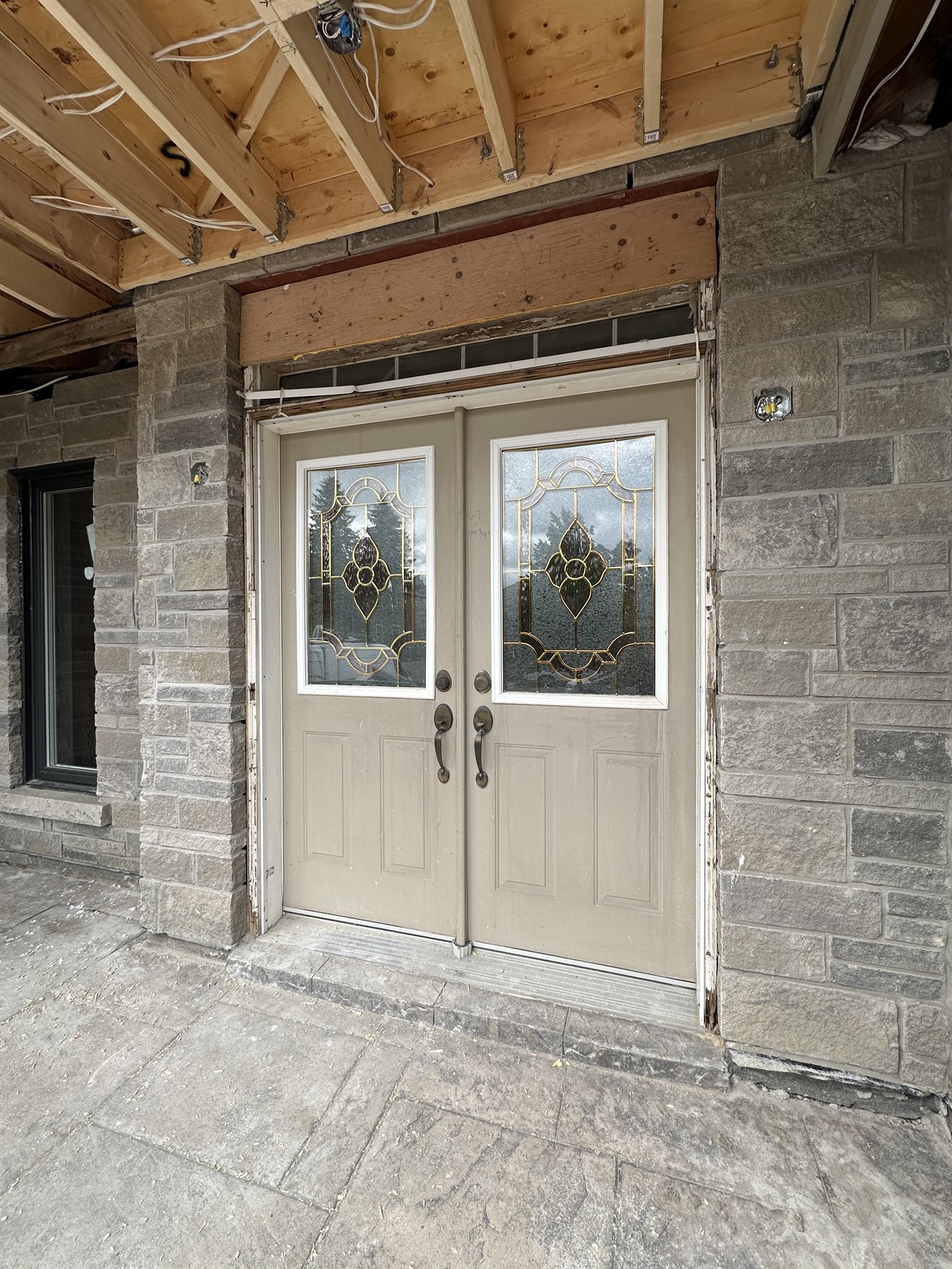 Beige double entry doors with decorative leaded glass in a stone porch