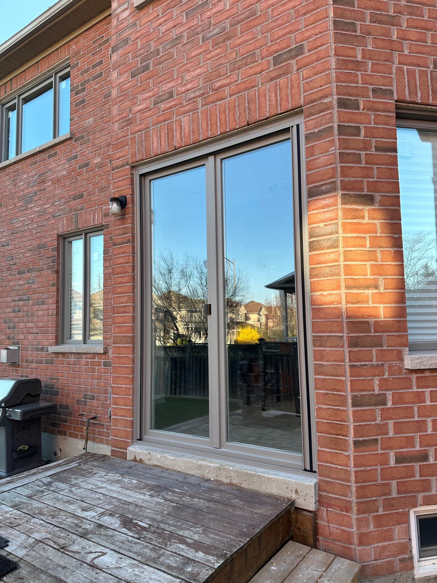 Beige-framed two-panel European door with full-height glass set in a red brick rear wall beside a wood deck
