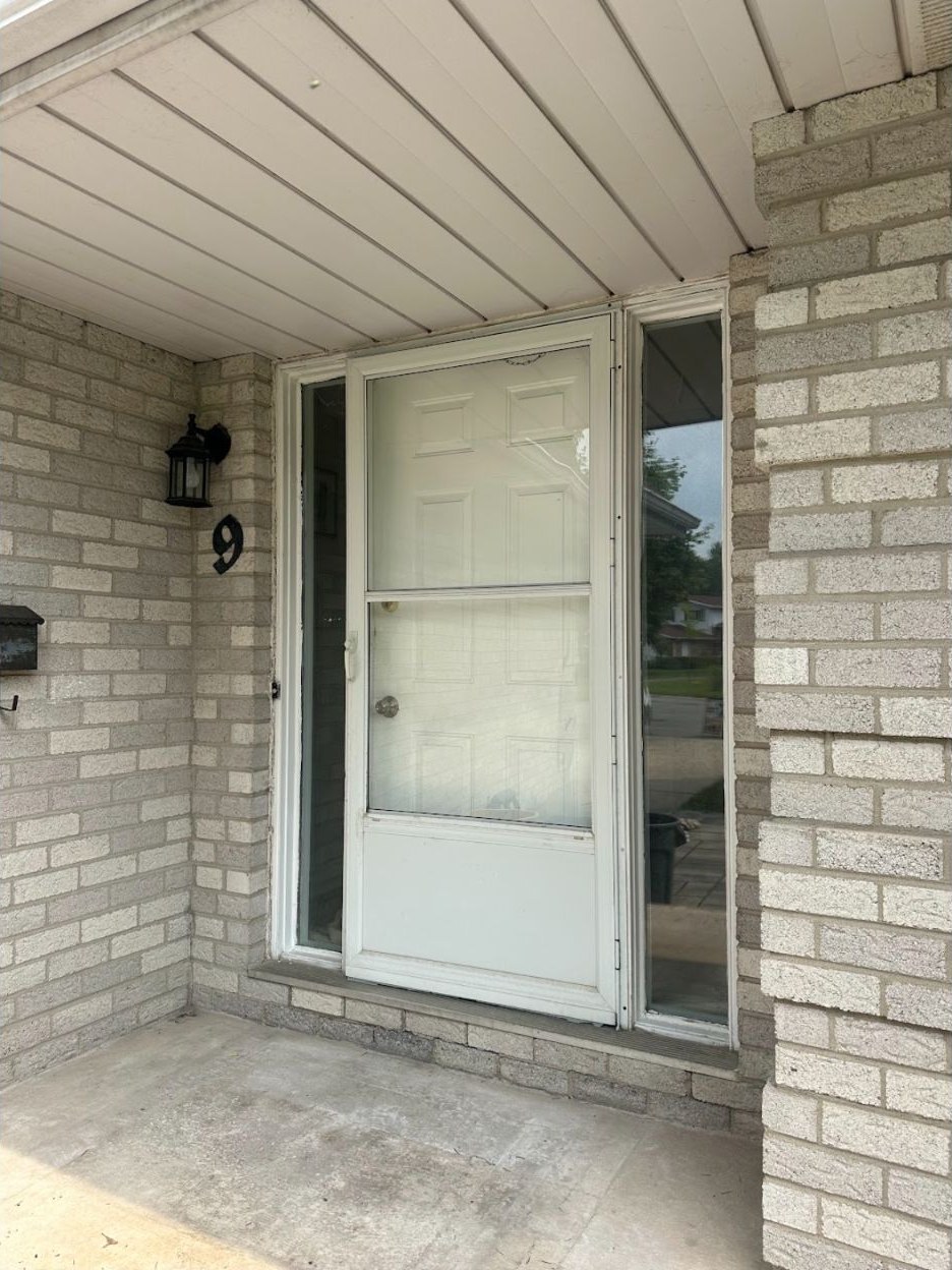 Older white entry door with a storm door and sidelites in a light brick porch